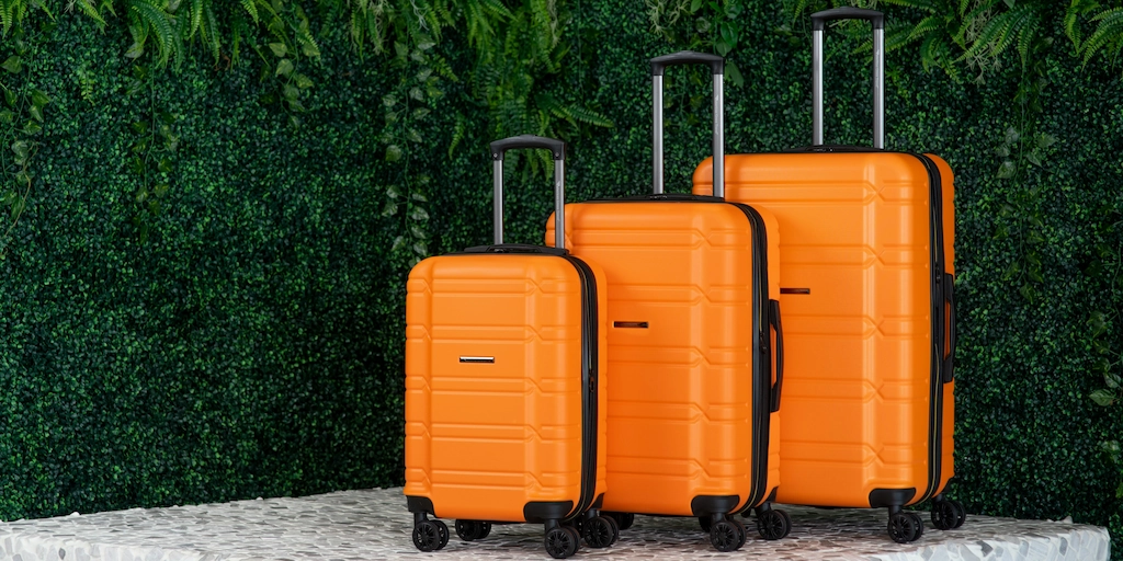 Orange suitcases lined up with a green plant wall in the background
