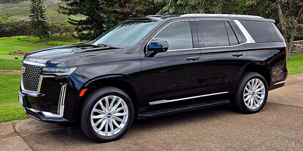 Cadillac Escalade by Maui Luxe parked on a Maui driveway with mountain backdrop.