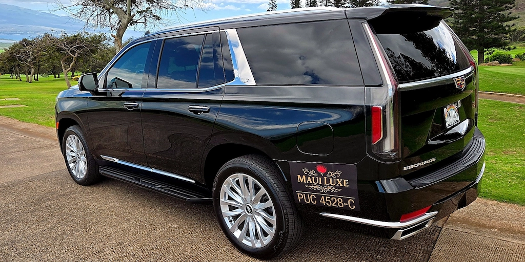 Rear three-quarter view of the Maui Luxe Cadillac Escalade with scenic Maui backdrop.